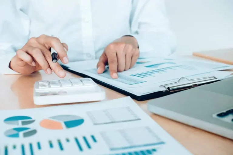 Contador revisa informes con gráficos y calculadora en una asesoría contable y tributaria